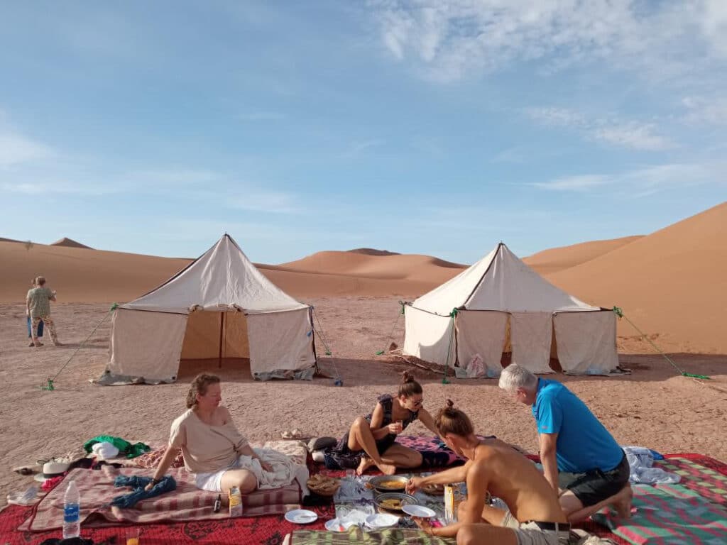 group of people in the desert, eating a meal at their camp